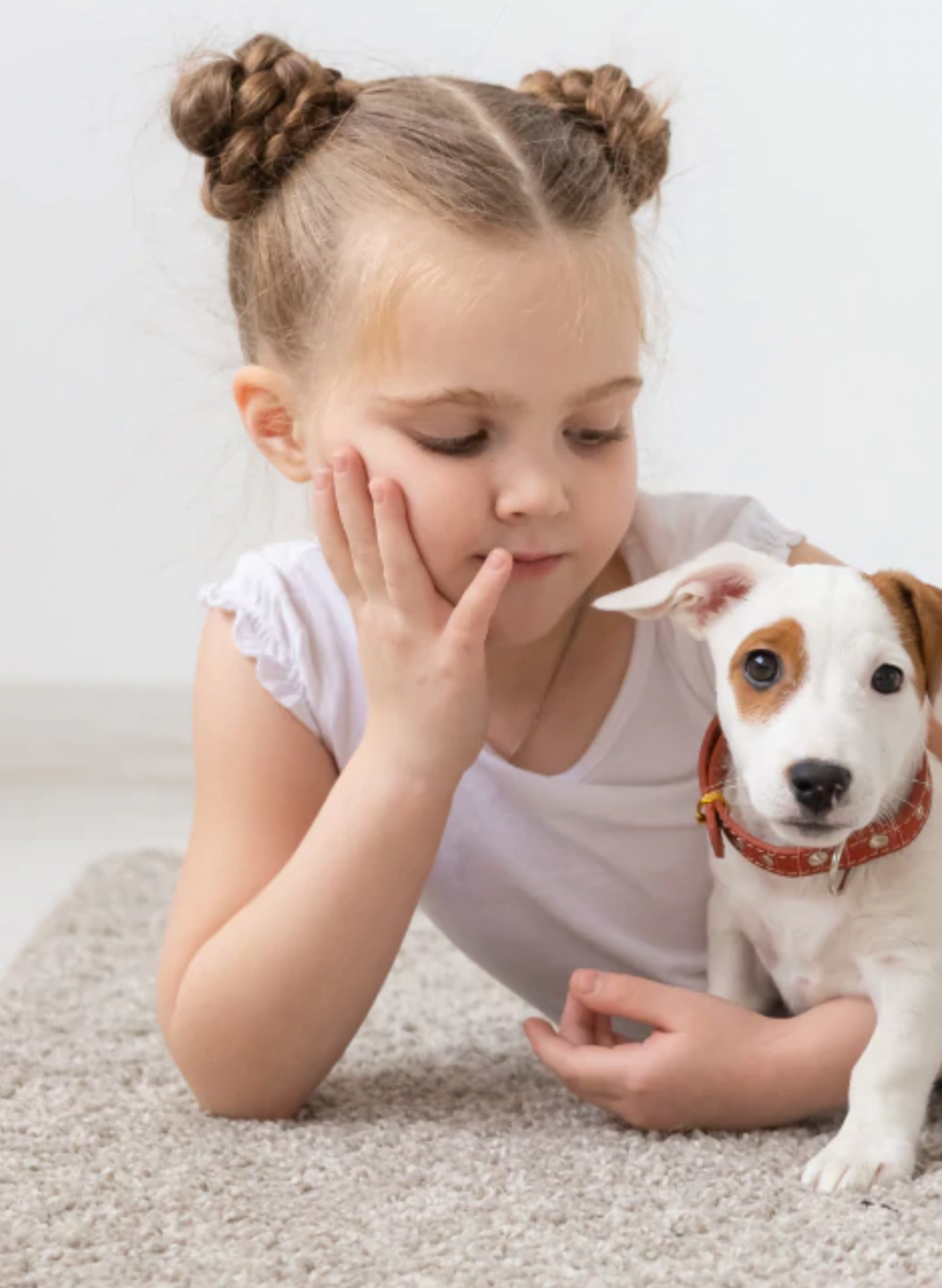A young girl hugging her small dog, both lying on a carpet rug.
