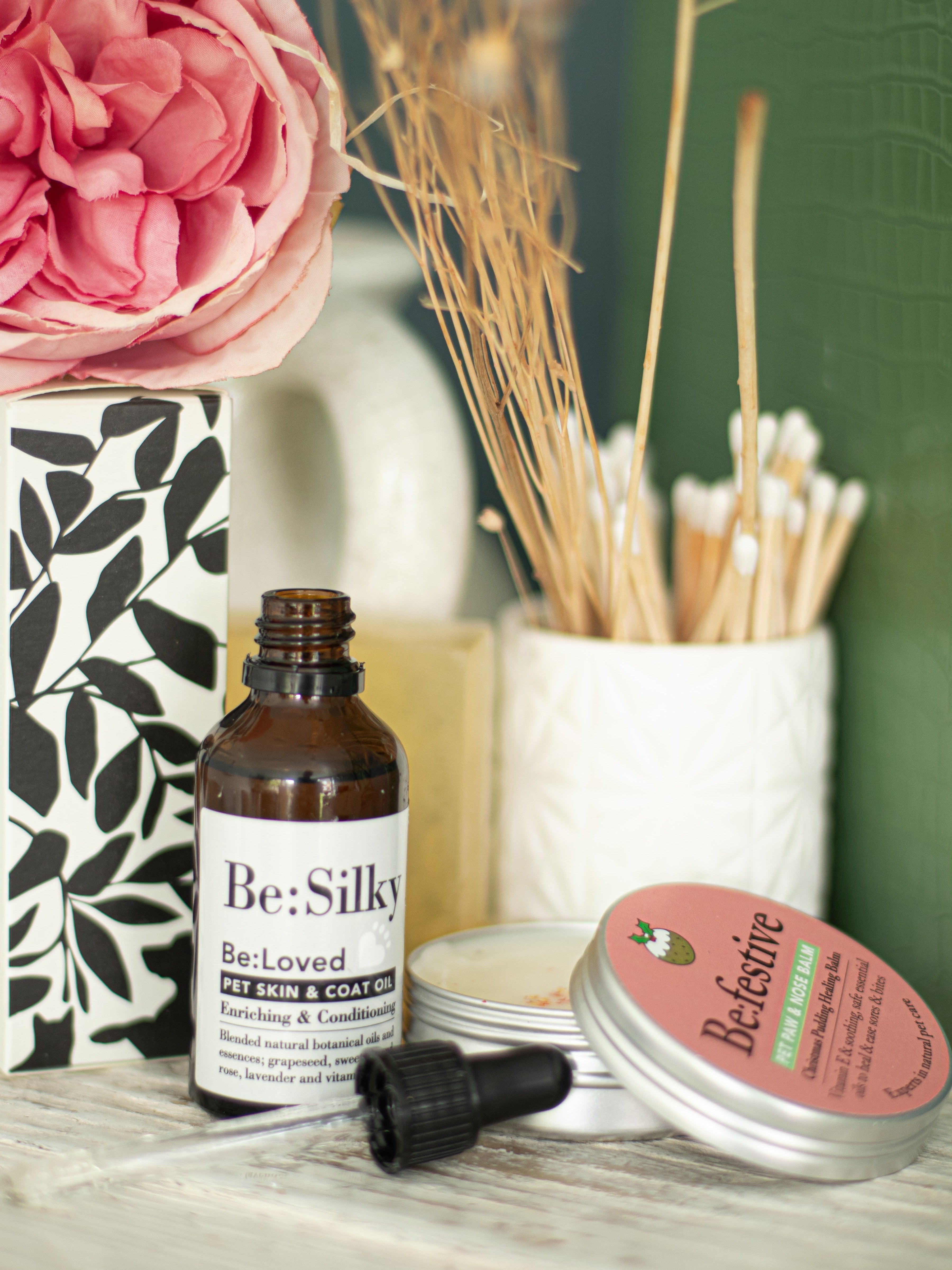 Lifestyle shot of Be:Silky and Be:Festive on a desk with flowers in the background